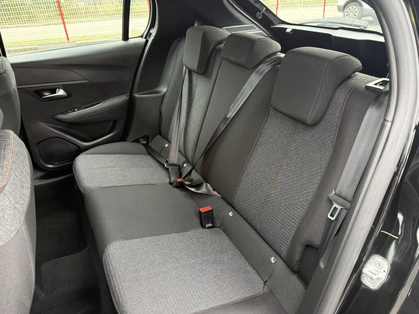 Vue intérieure côté droit des sièges arrière en tissu gris et noir avec surpiqûres orange d’une Peugeot 208 noire Perla Nera.