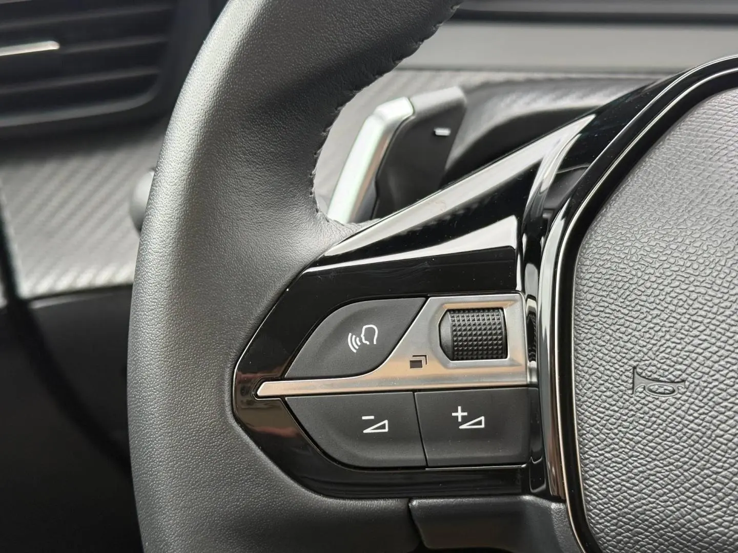 Gros plan sur les commandes vocales et volume sur le volant noir de la Peugeot 208 hybride 2025.