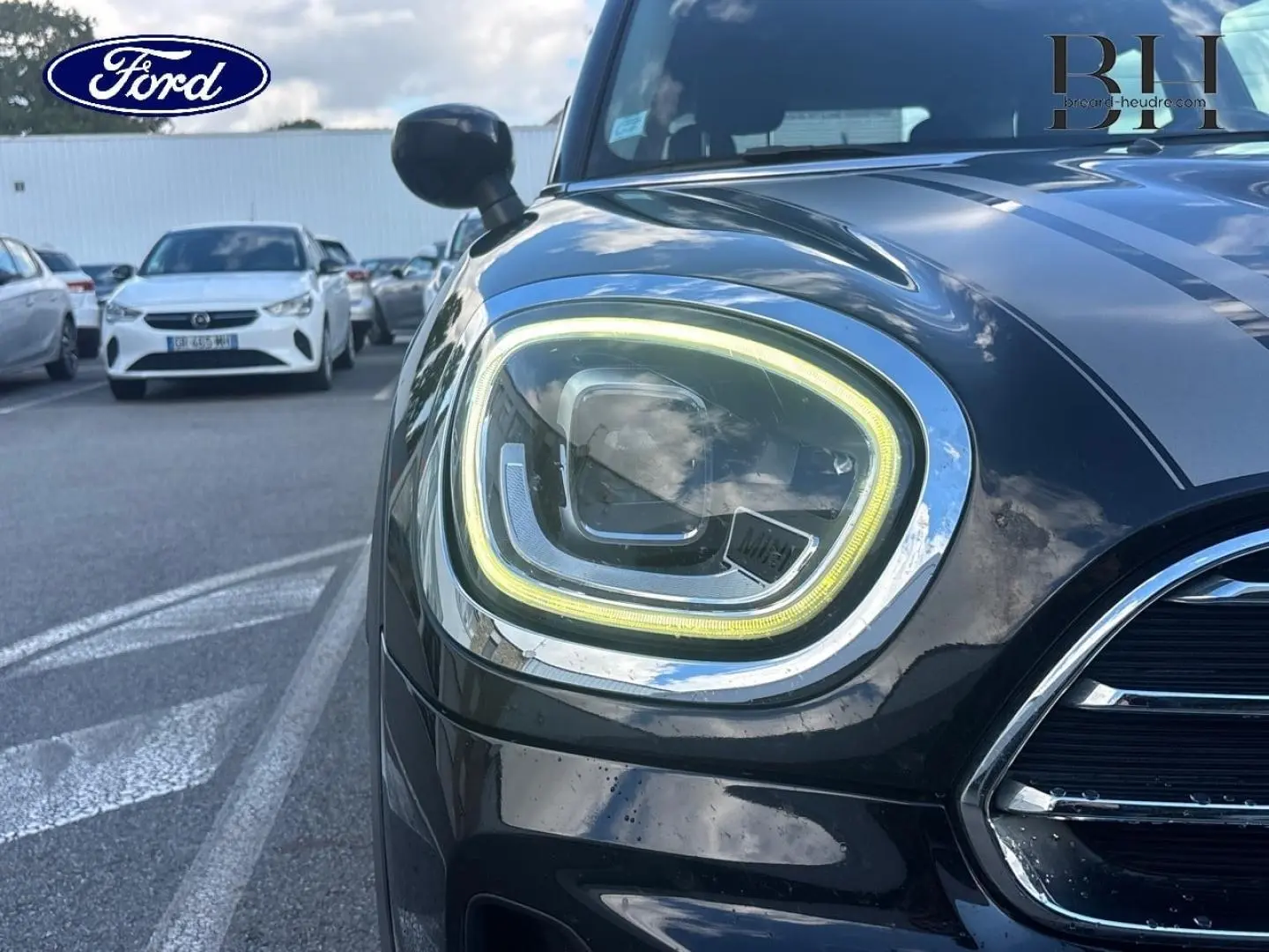 Gros plan sur le phare avant gauche allumé d’une MINI Countryman Cooper D noire avec bandes grises sur le capot.