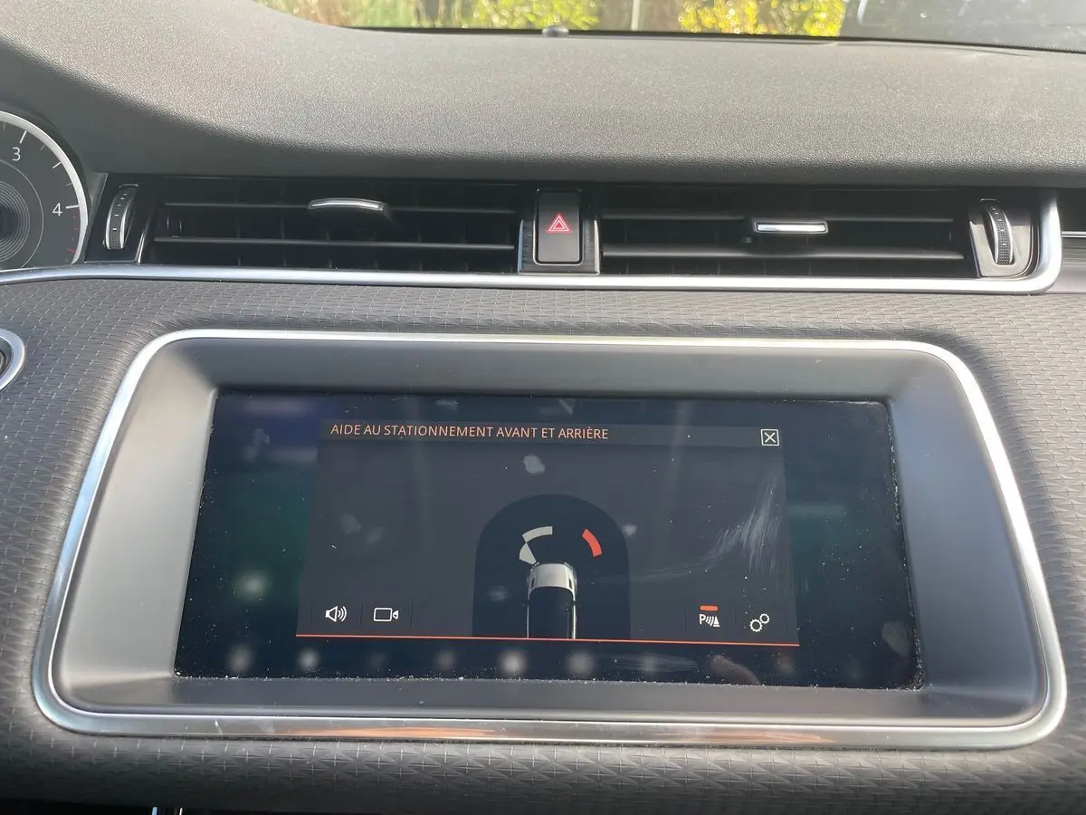 Écran tactile central du Range Rover Evoque blanc 2020 montrant l'aide au stationnement avant et arrière.