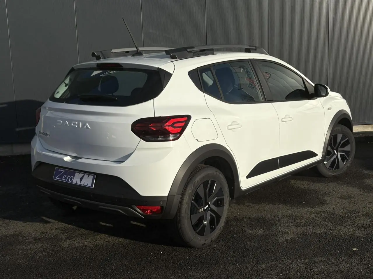 Vue 3/4 arrière droite d'une Dacia Sandero Stepway blanche Glacier avec barres de toit et feux LED distinctifs.