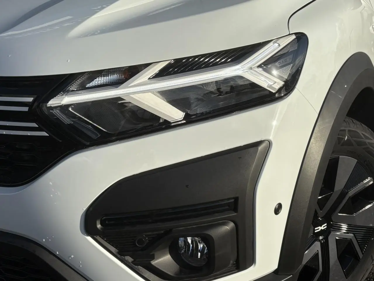 Gros plan sur l'avant droit blanc glacier du Dacia Sandero Stepway 2024, mettant en valeur le phare LED et la roue noire.