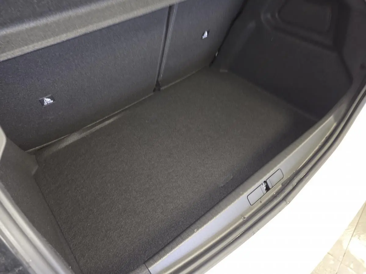 Vue rapprochée du coffre noir d’une Peugeot 208 blanche hybride, montrant le tapis de sol et la bordure du coffre.