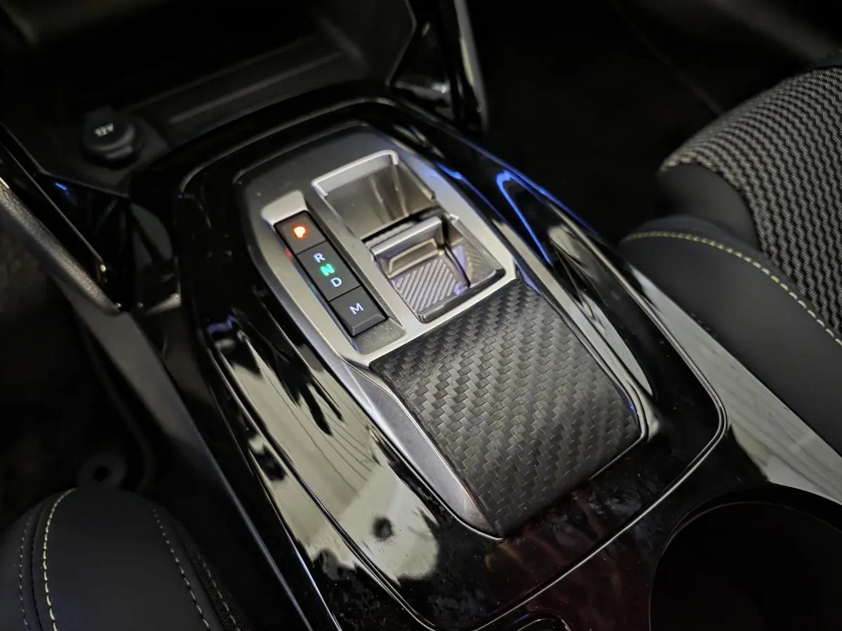 Gros plan sur la console centrale noire brillante avec sélecteur de boîte automatique et surpiqûres vertes du siège tissu Peugeot 208 GT blanc.