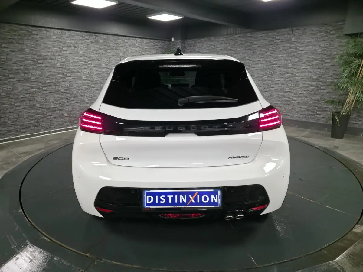 Vue arrière d'une Peugeot 208 blanche hybride 2025 avec feux arrière LED et bandeau noir brillant entre les feux.
