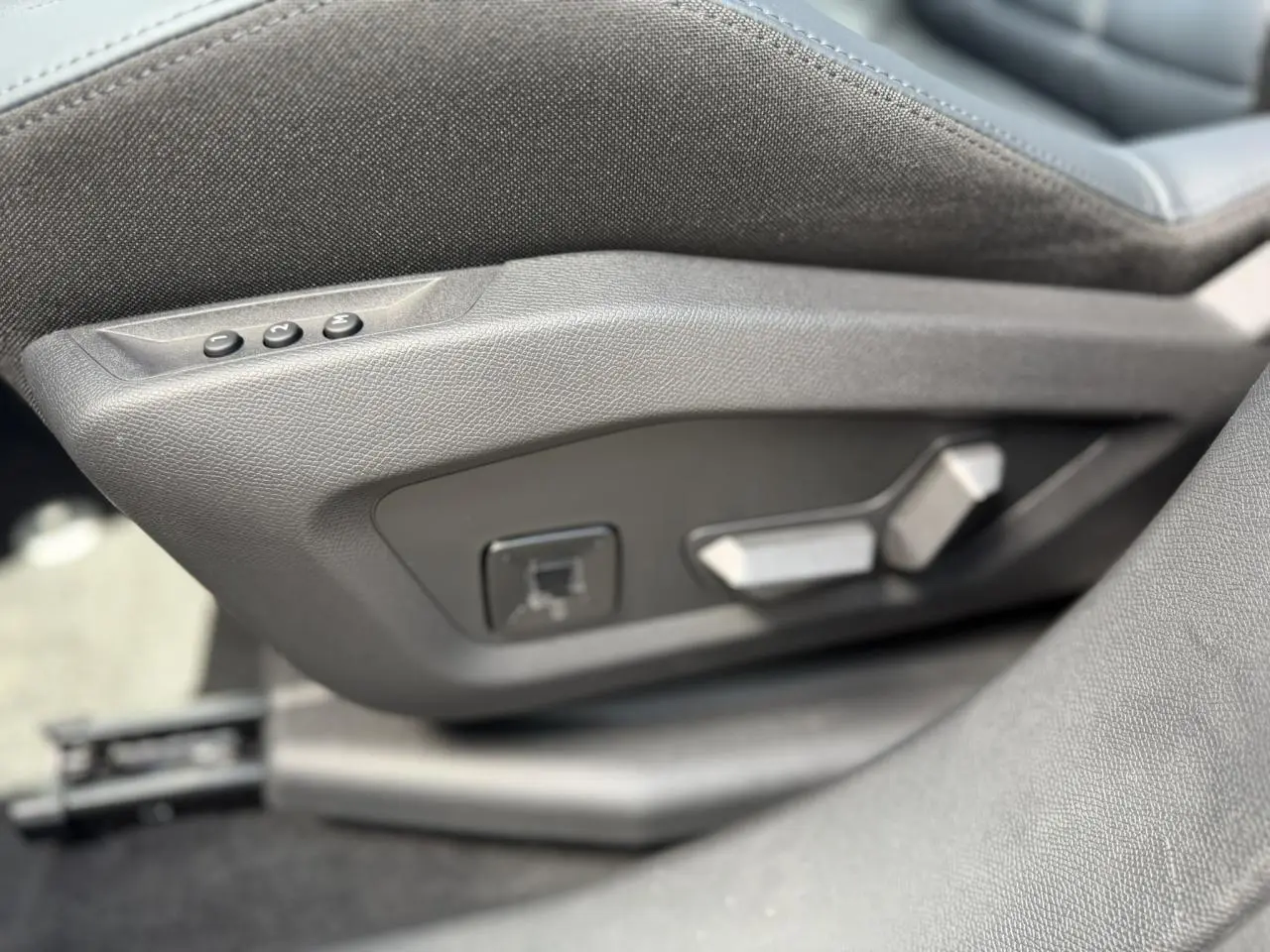 Détail des commandes électriques de réglage du siège conducteur en tissu gris dans une Citroën C5 Aircross.