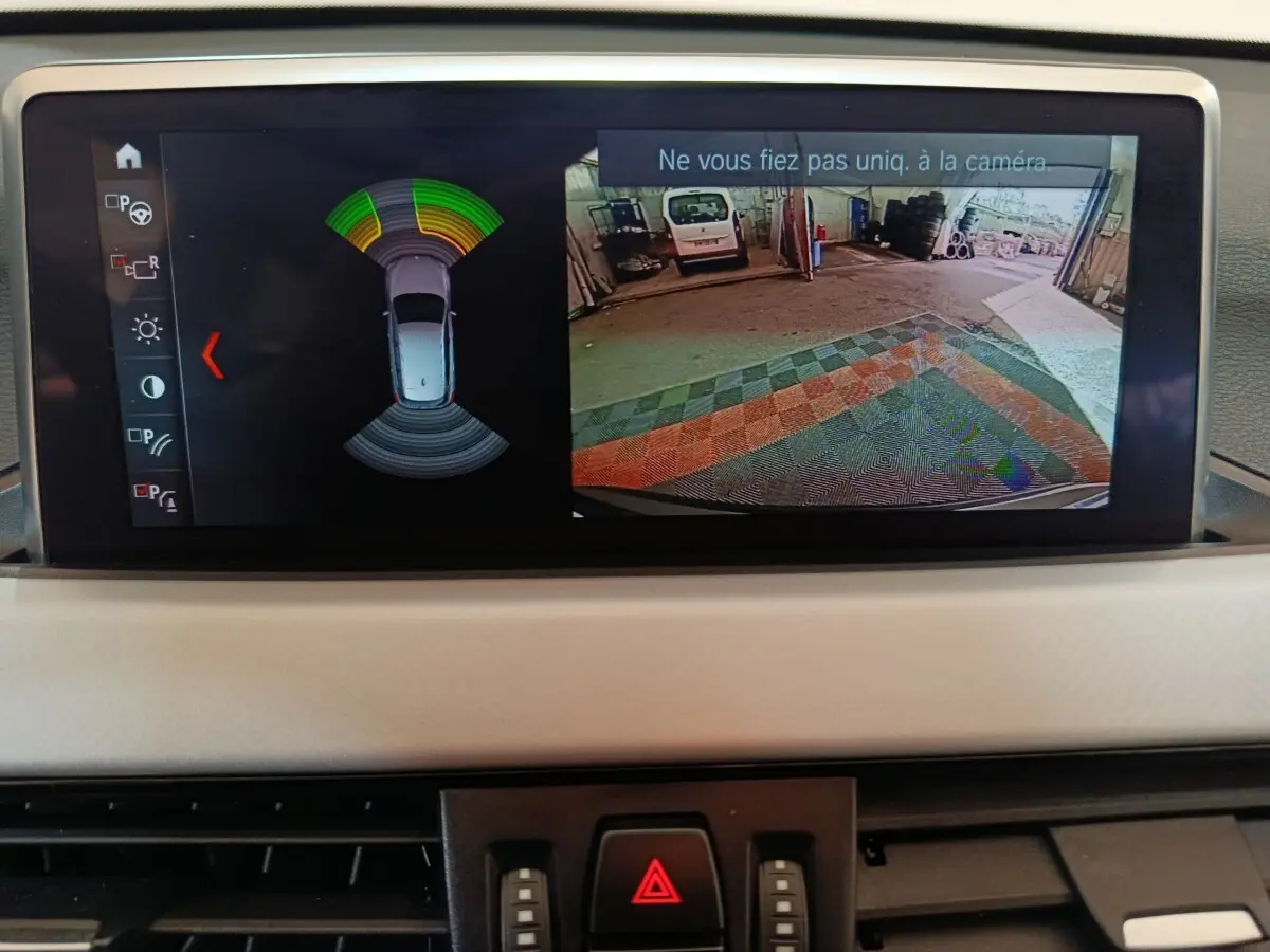 Écran central de BMW X1 sDrive18i 2021 montrant la caméra de recul et l’alerte de proximité en intérieur gris foncé.