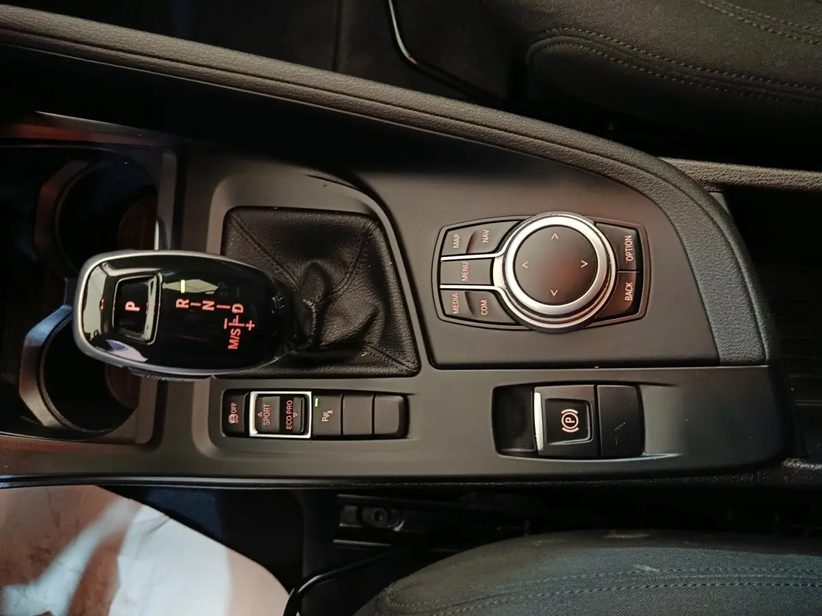 Vue rapprochée de la console centrale noire du BMW X1 sDrive18i Lounge avec levier de vitesses automatique et molette de contrôle.