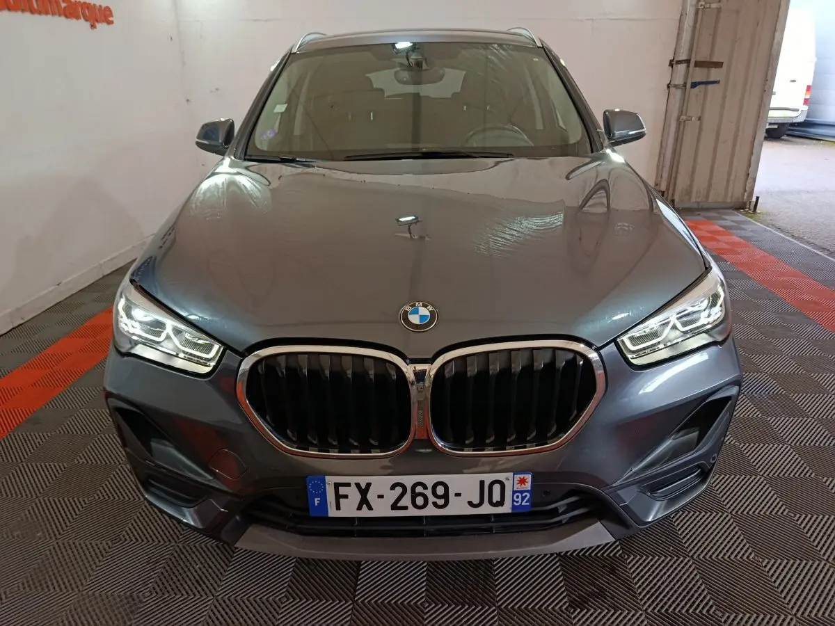 Vue avant d’un BMW X1 sDrive18i Lounge gris foncé avec calandre double haricot et phares LED allumés dans un garage.