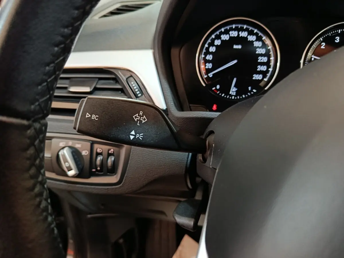 Gros plan sur la commande de clignotant et le tableau de bord noir d'une BMW X1 sDrive18i Lounge 2021.