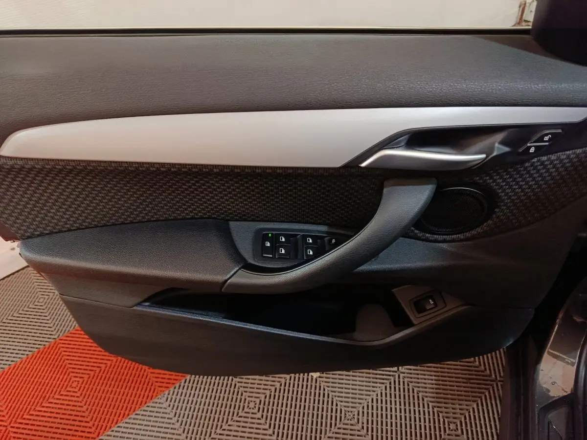Vue rapprochée de la porte avant gauche du BMW X1 gris foncé, avec commandes de vitres et poignée argentée.