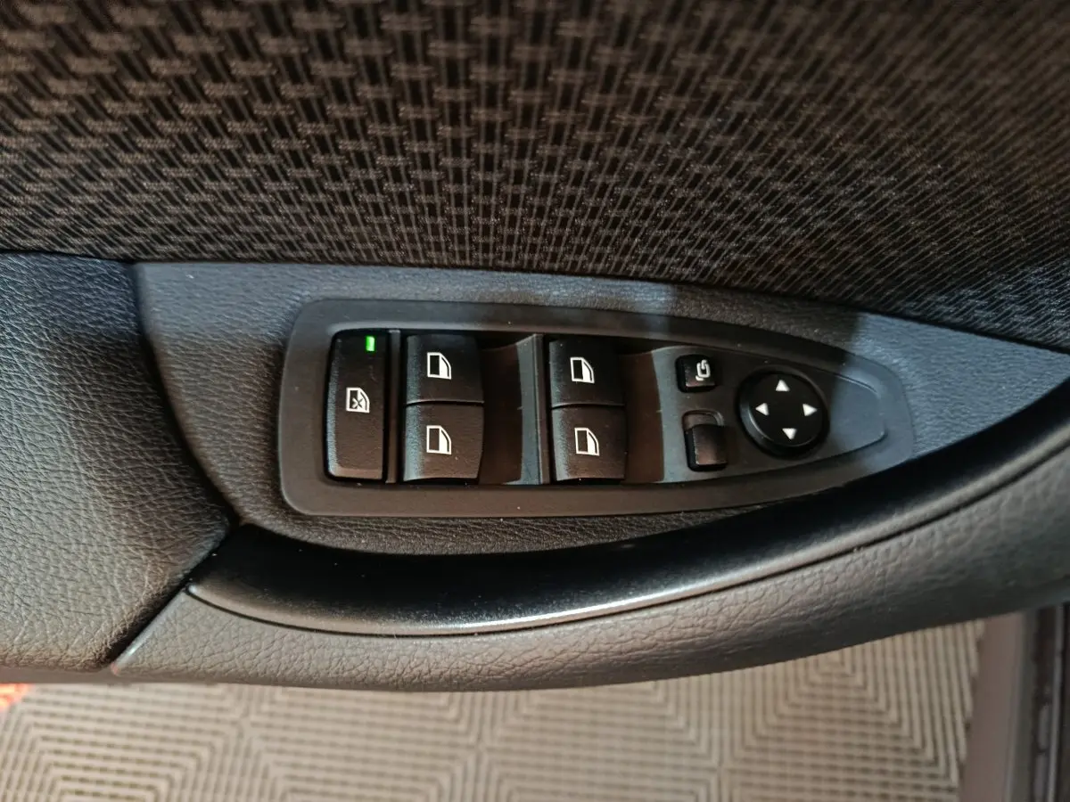 Gros plan sur les commandes de lève-vitres et rétroviseurs côté conducteur en plastique noir dans une BMW X1 gris foncé.