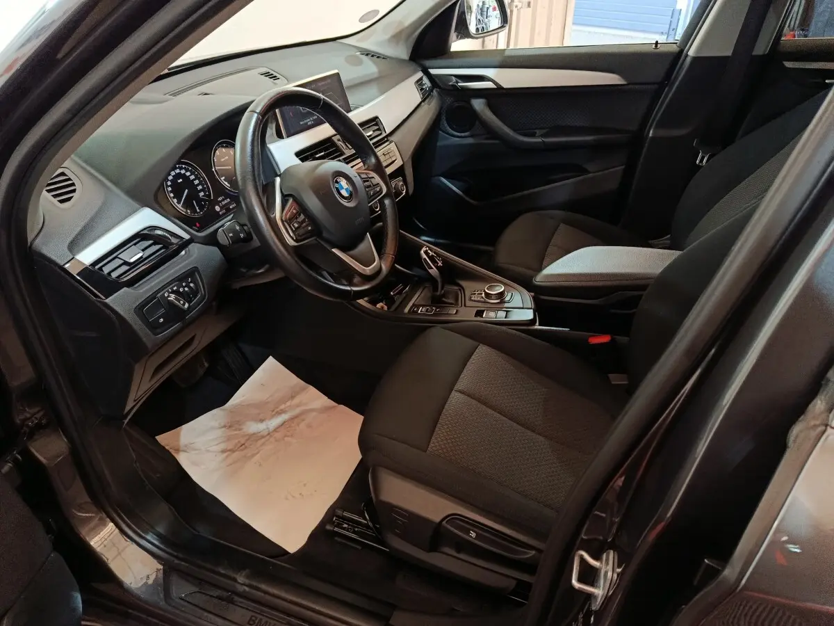 Vue intérieure côté conducteur du BMW X1 gris foncé, montrant le volant cuir multifonctions et la console centrale moderne.