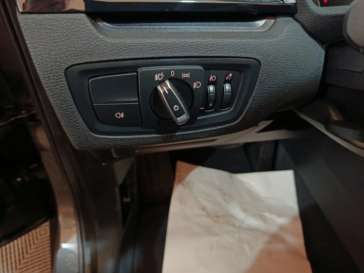 Gros plan sur les commandes d'éclairage du tableau de bord d'un BMW X1 sDrive18i Lounge gris foncé, côté conducteur.