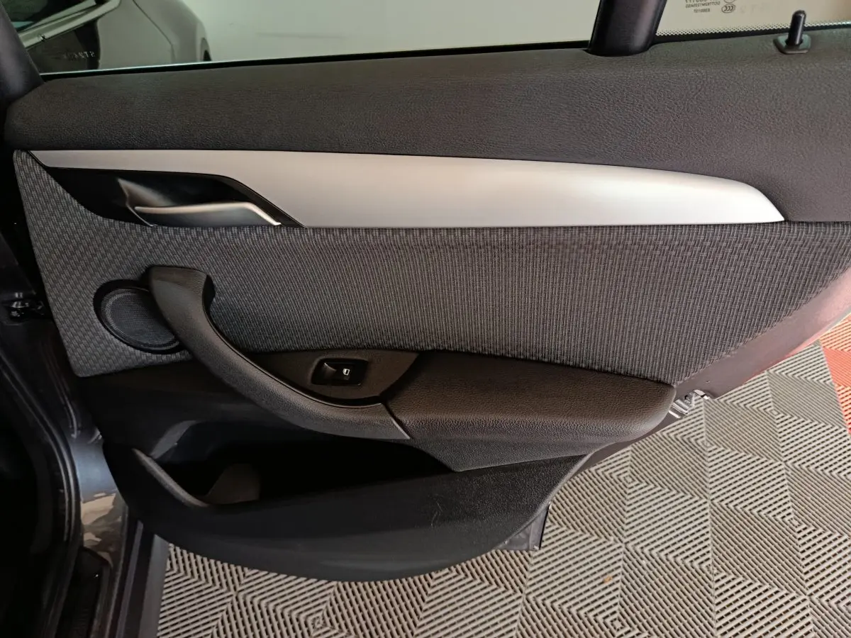 Gros plan sur la porte arrière gauche intérieure du BMW X1 sDrive18i Lounge 2021, avec garniture grise et poignée noire.