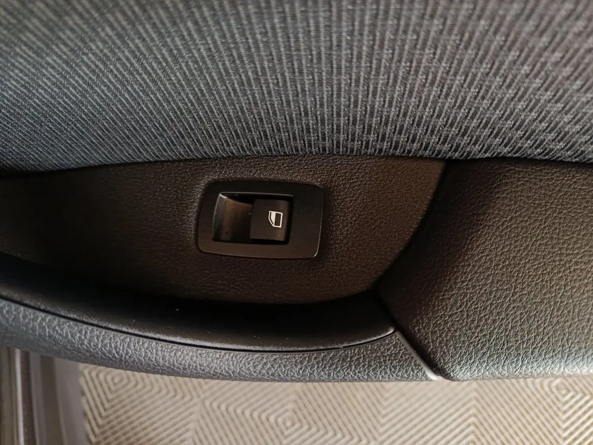 Gros plan sur l'interrupteur de lève-vitre côté porte intérieure d'une BMW X1 gris foncé sDrive18i Lounge 2021.