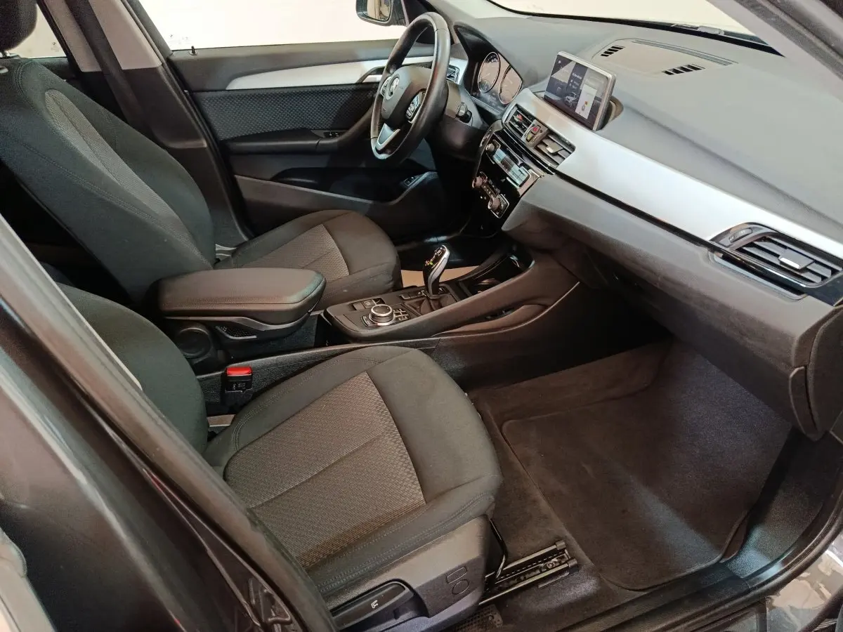 Intérieur avant de la BMW X1 sDrive18i Lounge 2021, vue côté conducteur, sièges tissu gris et tableau de bord moderne.