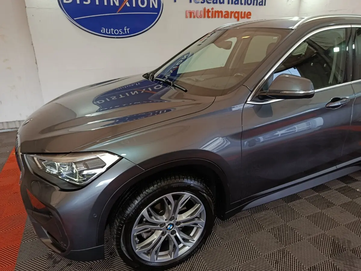 BMW X1 sDrive18i gris foncé vue 3/4 avant côté gauche, avec jante alliage et phares LED distinctifs.