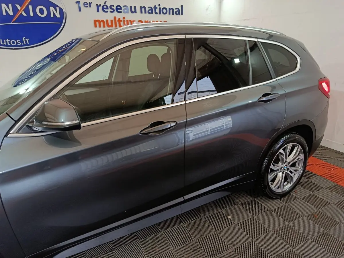 Vue latérale droite d'un BMW X1 sDrive18i Lounge gris foncé, avec jantes alliage et rails de toit noirs visibles.