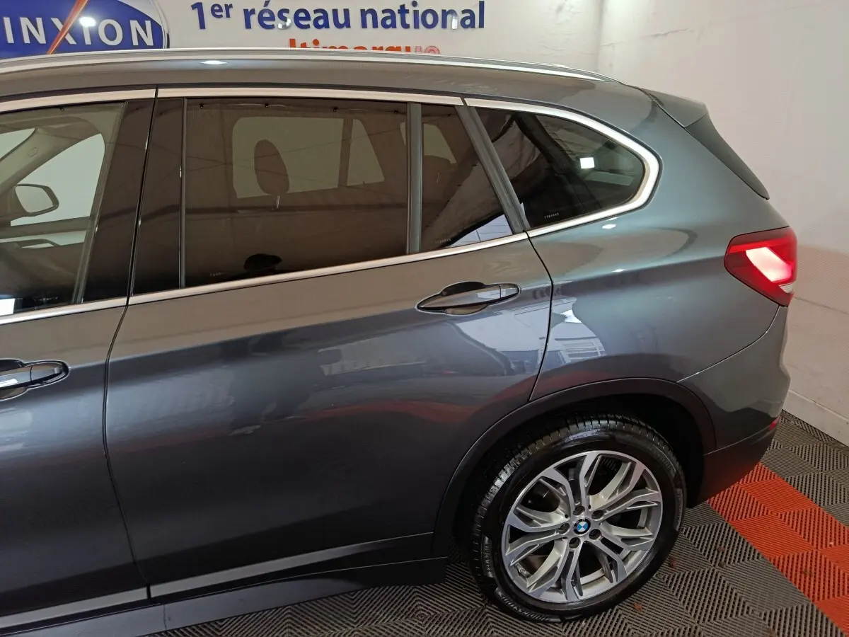 Vue latérale droite sur l'arrière d'un BMW X1 sDrive18i Lounge gris foncé avec feu arrière allumé et jante alliage.