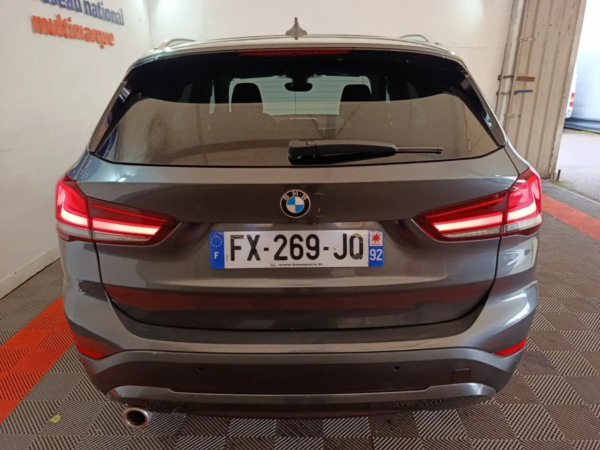 Vue arrière d’un BMW X1 gris foncé avec feux arrière allumés et plaque d’immatriculation française visible.