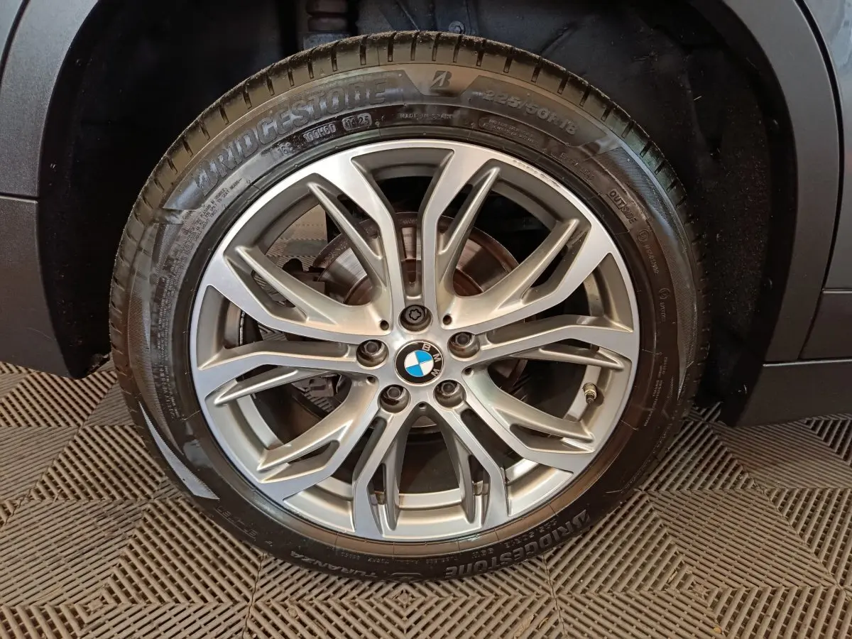 Gros plan sur la roue avant droite d’un BMW X1 gris foncé, montrant le pneu Bridgestone et l’aile du véhicule.