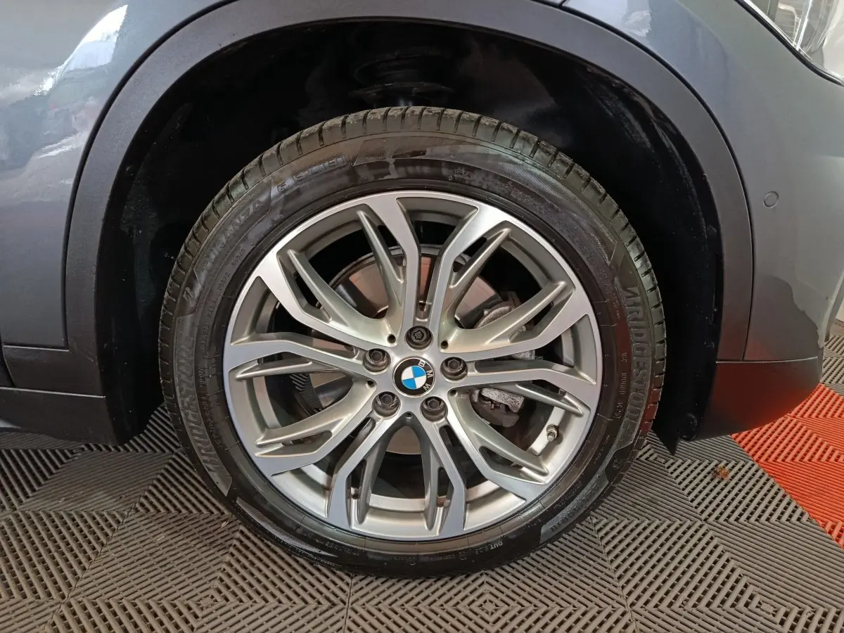 Gros plan sur la roue avant droite d’un BMW X1 gris foncé, mettant en valeur la jante alliage et le logo BMW central.