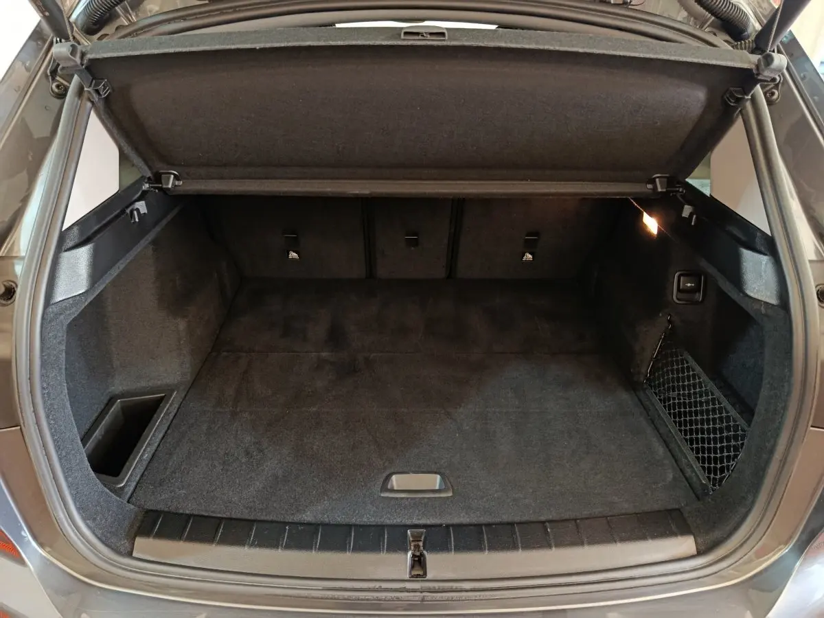 Coffre ouvert d’une BMW X1 sDrive18i Lounge gris foncé, vue de l’arrière montrant l’espace de chargement et le cache-bagages.
