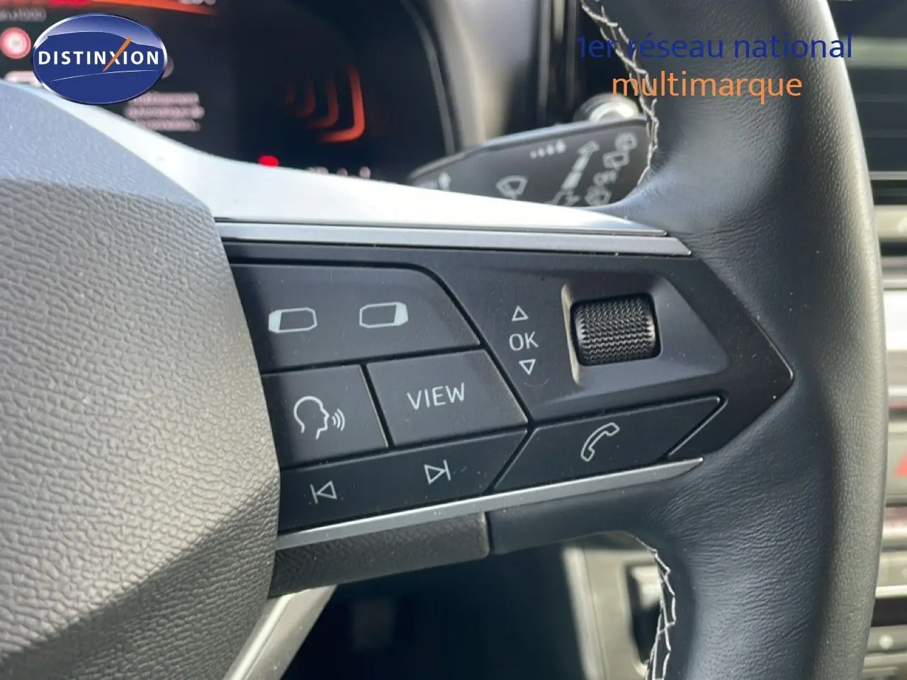 Gros plan sur les commandes gauche du volant en cuir noir du SEAT Ibiza bleu Fjord 2025, avec boutons multifonctions.