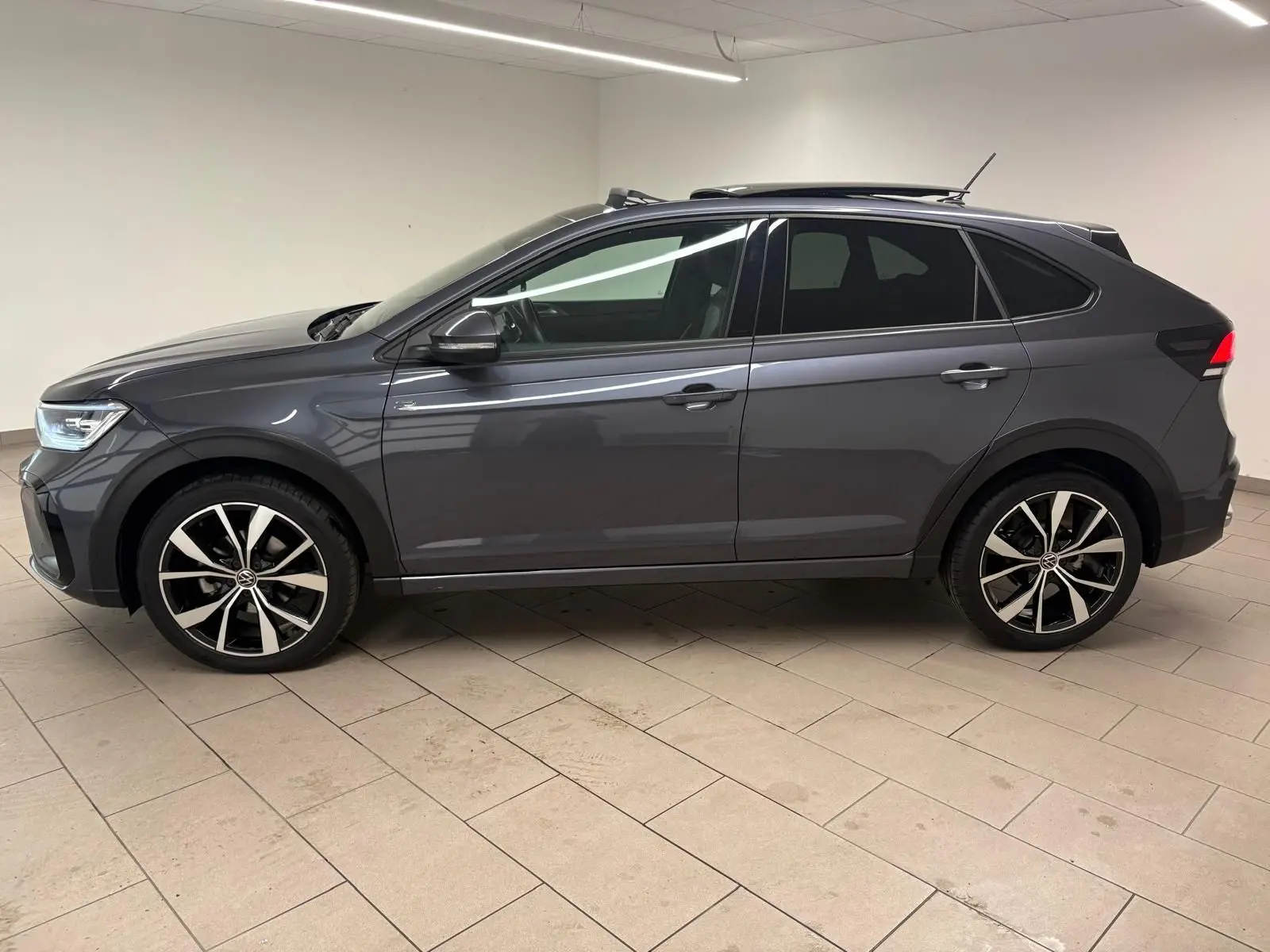 Volkswagen Taigo gris cendré vue de profil côté gauche, avec jantes noires brillantes et toit ouvrant électrique.