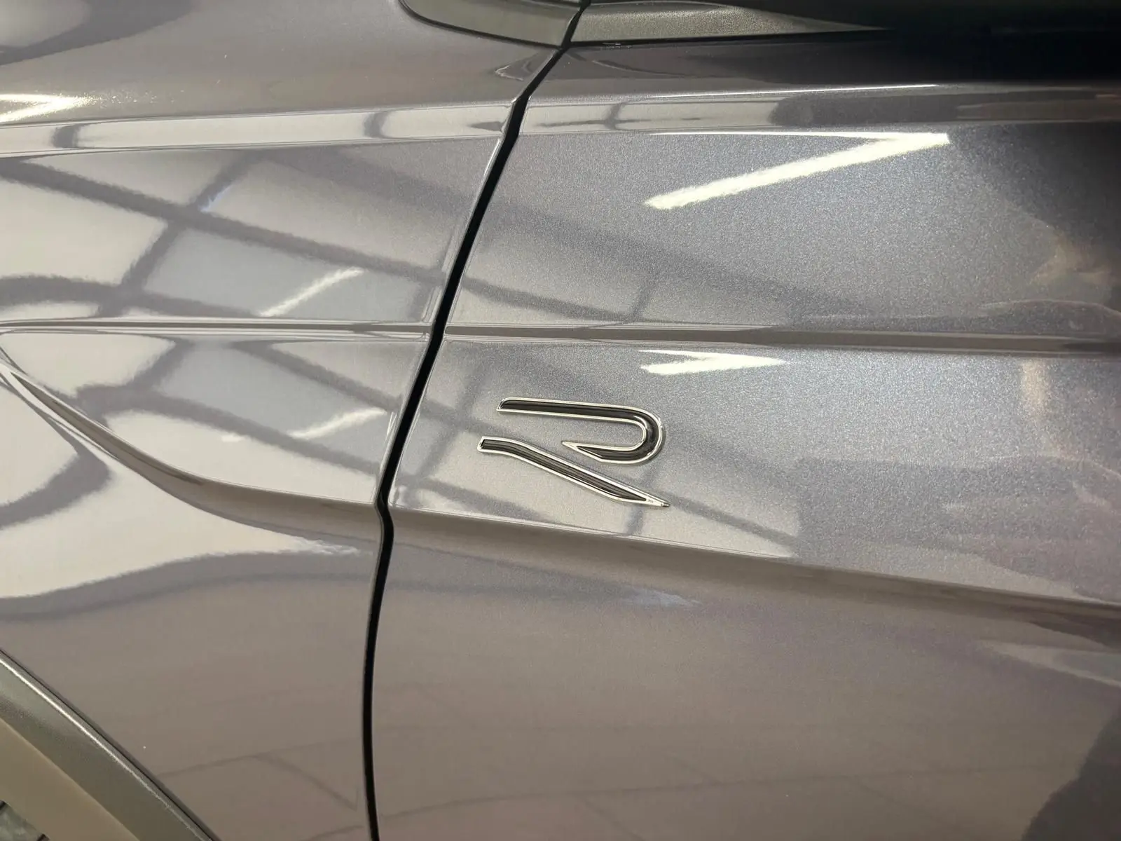 Gros plan sur l'emblème R sur la porte avant gauche du Volkswagen Taigo gris cendré métallisé.