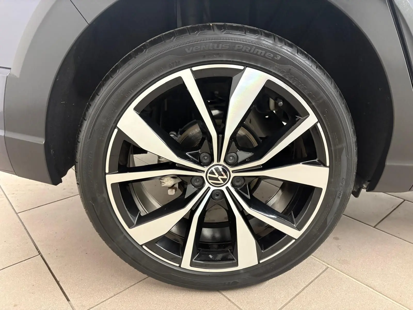 Gros plan sur la jante alliage noir et argent 18 pouces du Volkswagen Taigo gris cendré, détail du pneu et logo VW au centre.