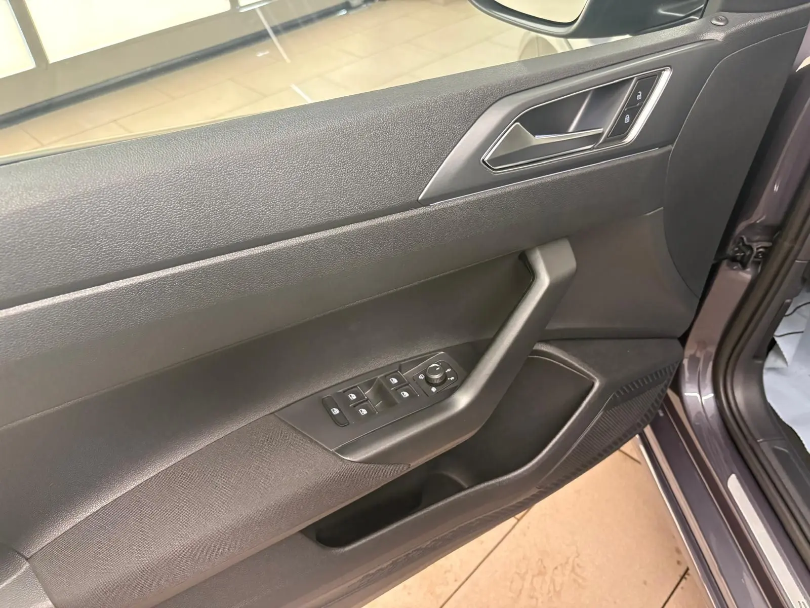 Vue rapprochée de la porte avant gauche du Volkswagen Taigo gris cendré, montrant les commandes des vitres et le verrouillage.