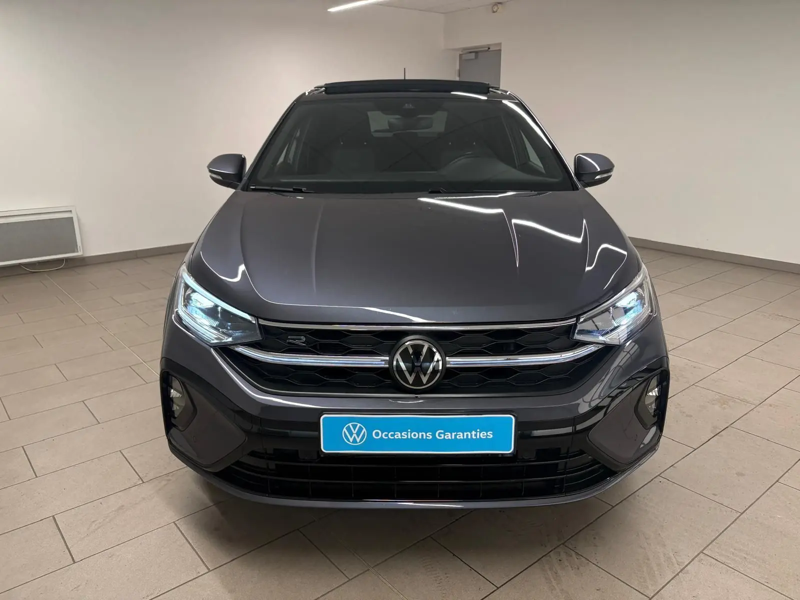 Vue avant d'un Volkswagen Taigo gris cendré 2024 avec calandre R-Line et toit ouvrant en intérieur neutre.