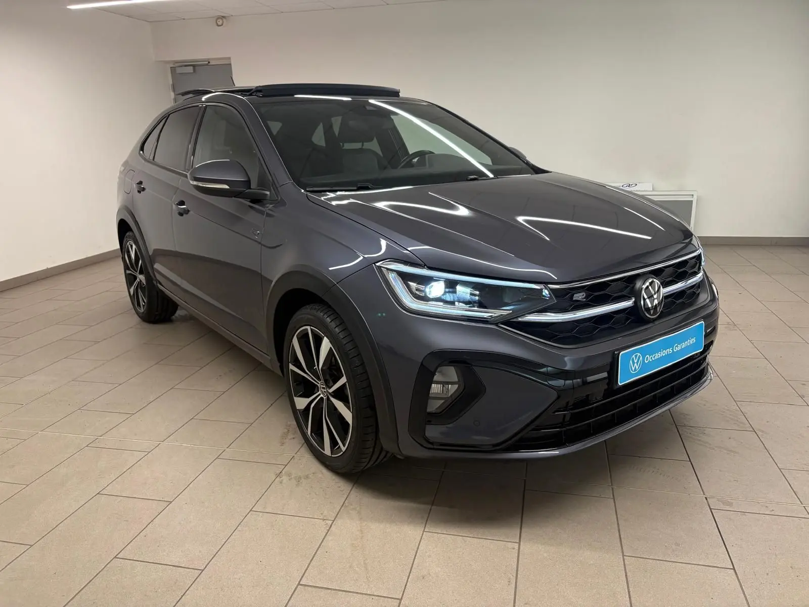 Volkswagen Taigo 1.5 TSI R-Line gris cendré en 3/4 avant droit avec toit ouvrant et jantes noires brillantes.