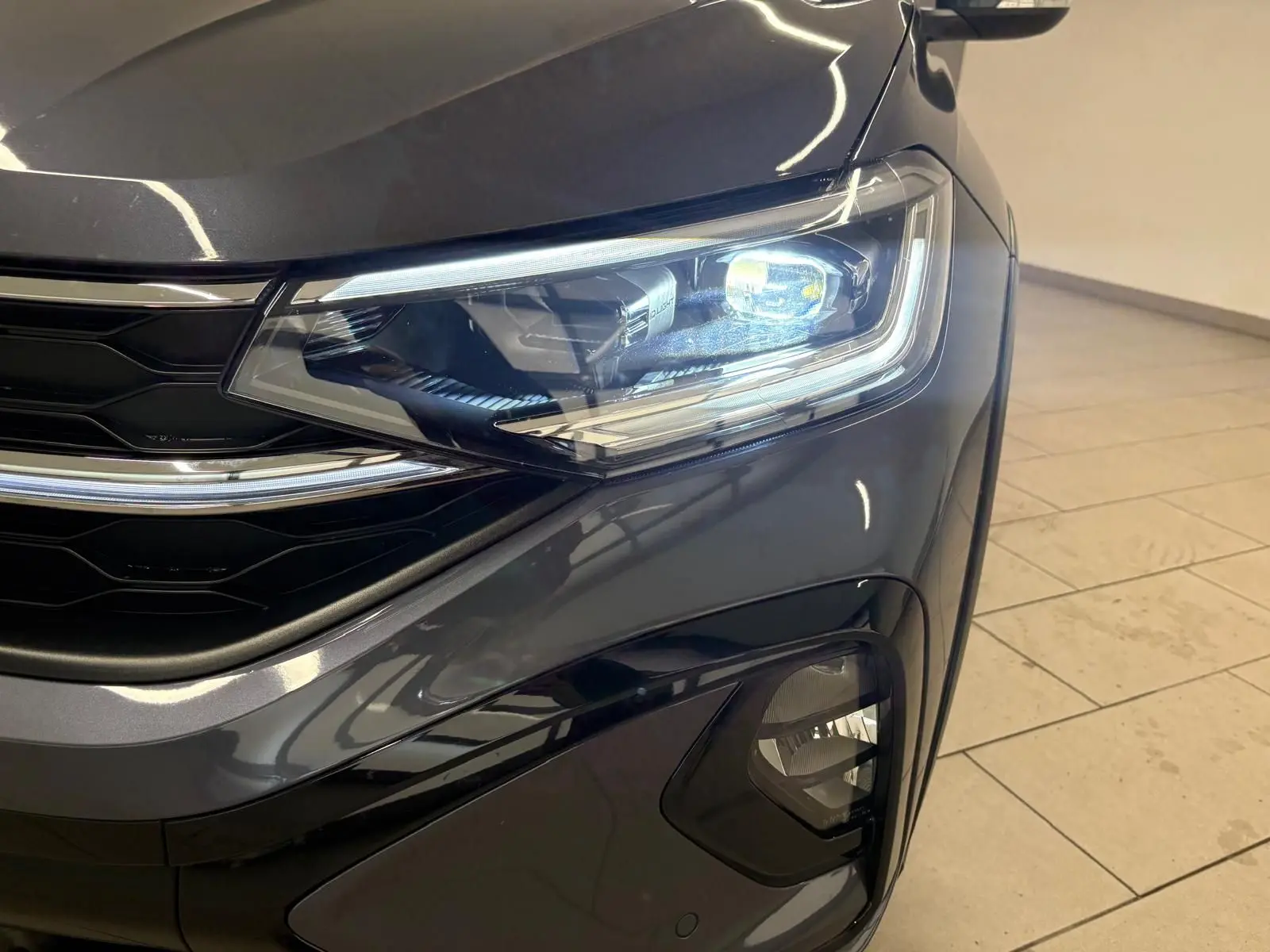Gros plan sur le phare avant droit du Volkswagen Taigo gris cendré 2024 avec détails lumineux et calandre noire brillante.