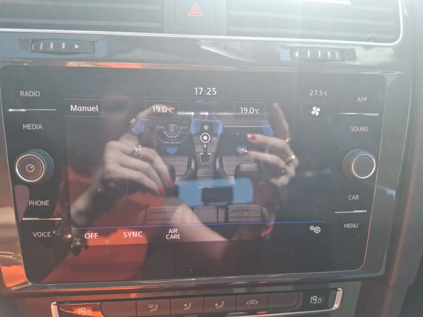 Écran tactile central de la Volkswagen Golf 2019 montrant la climatisation bi-zone avec reflet des mains au-dessus.