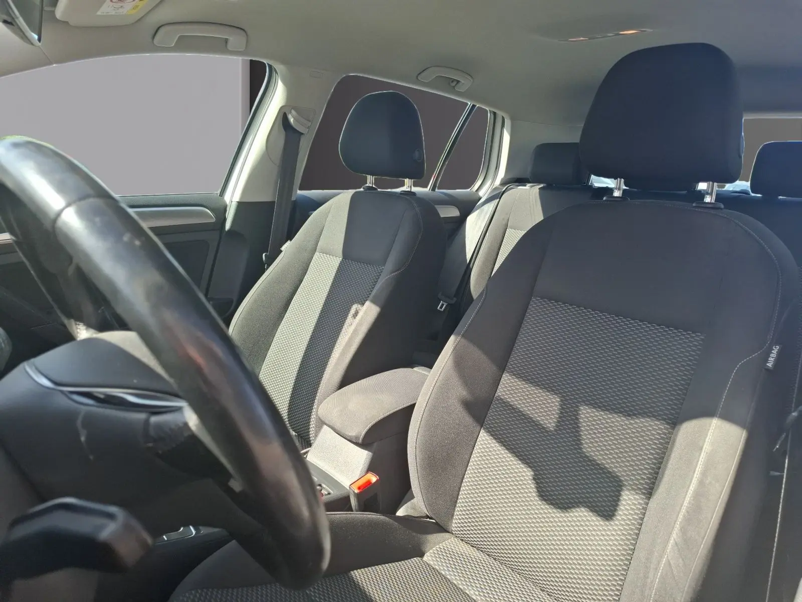 Vue intérieure de la Volkswagen Golf 2019, sièges avant en tissu gris et volant côté gauche visible.