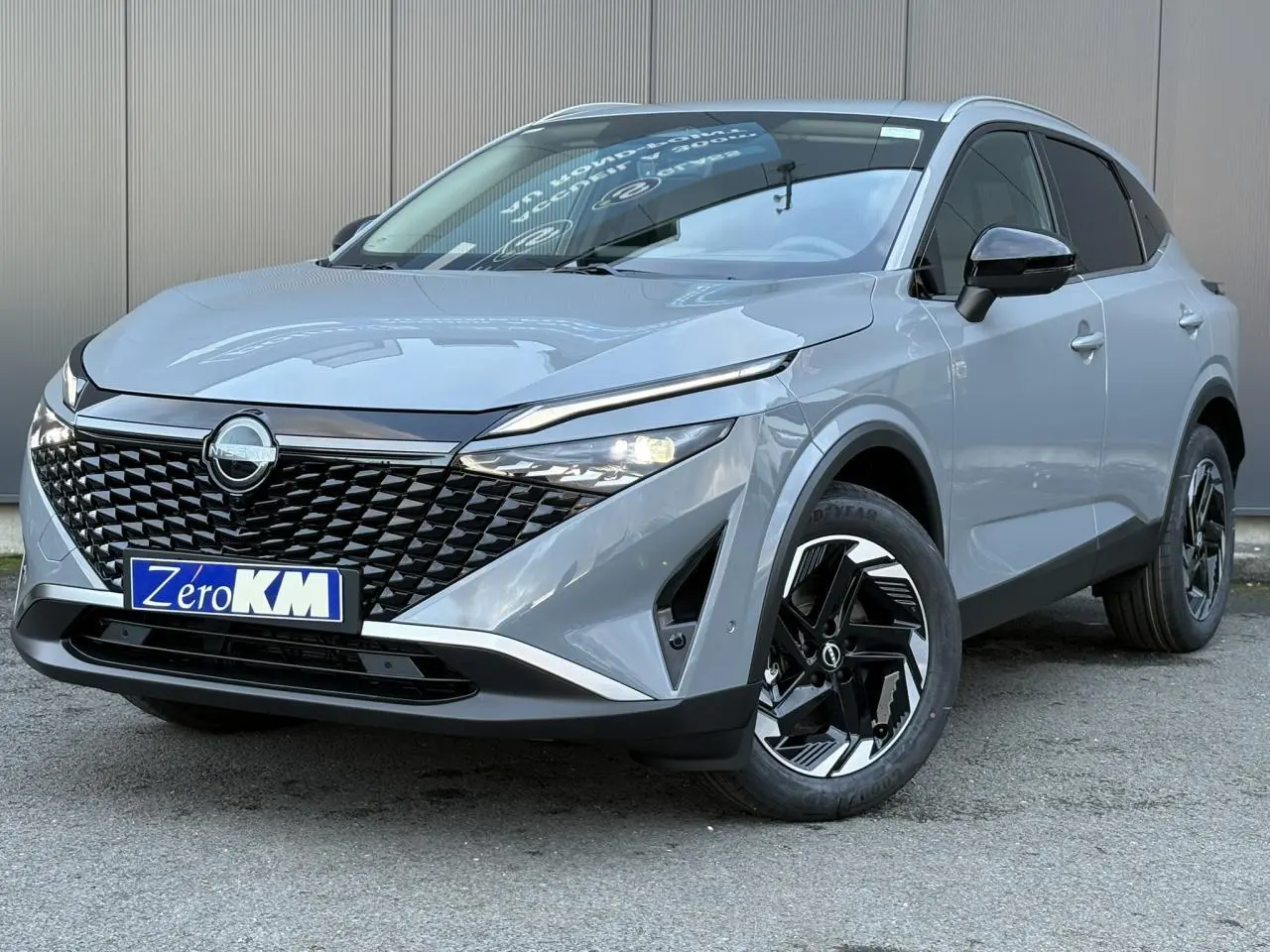 Vue 3/4 avant droit du Nissan Qashqai III gris Ceramic avec calandre noire et jantes alliage bicolores.