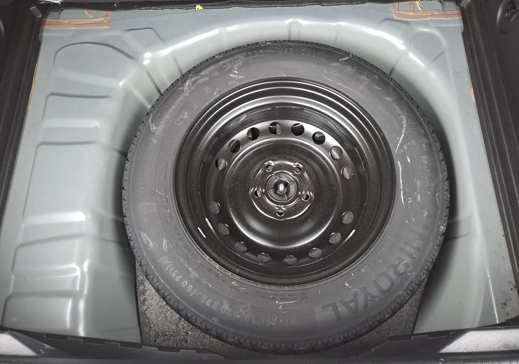 Vue plongeante sur la roue de secours noire logée dans le coffre gris clair du Renault Captur bleu marine 2022.