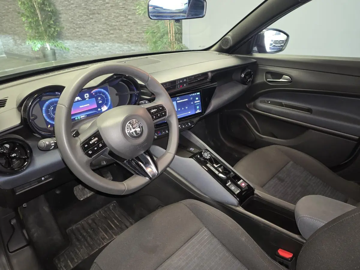 Vue intérieure côté conducteur de l'Alfa Romeo Junior 1.2 hybride 2025 avec tableau de bord digital et sellerie Icona grise.