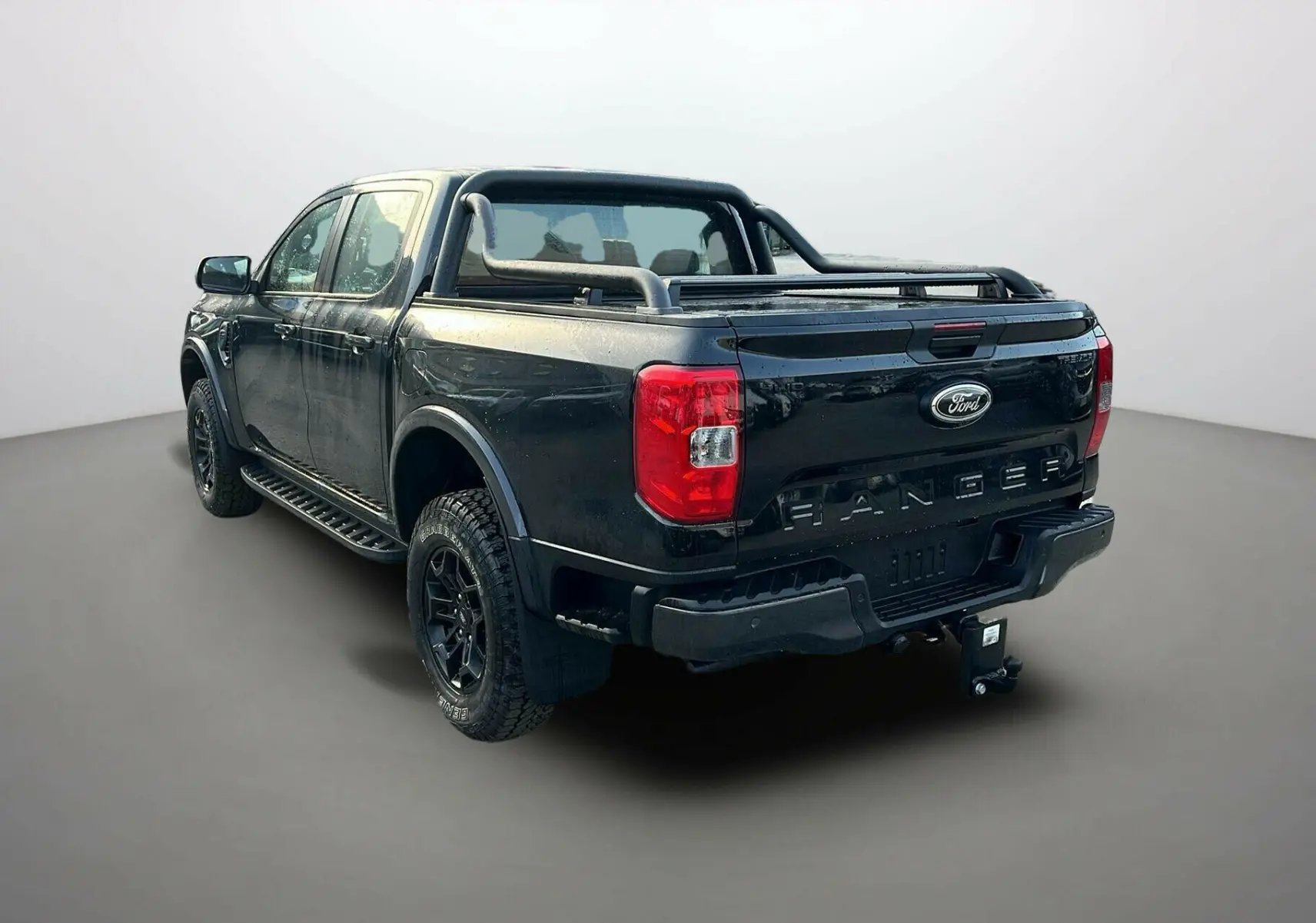Ford Ranger 2025 noir agate en 3/4 arrière droit, avec attelage, arceaux noirs et benne couverte.