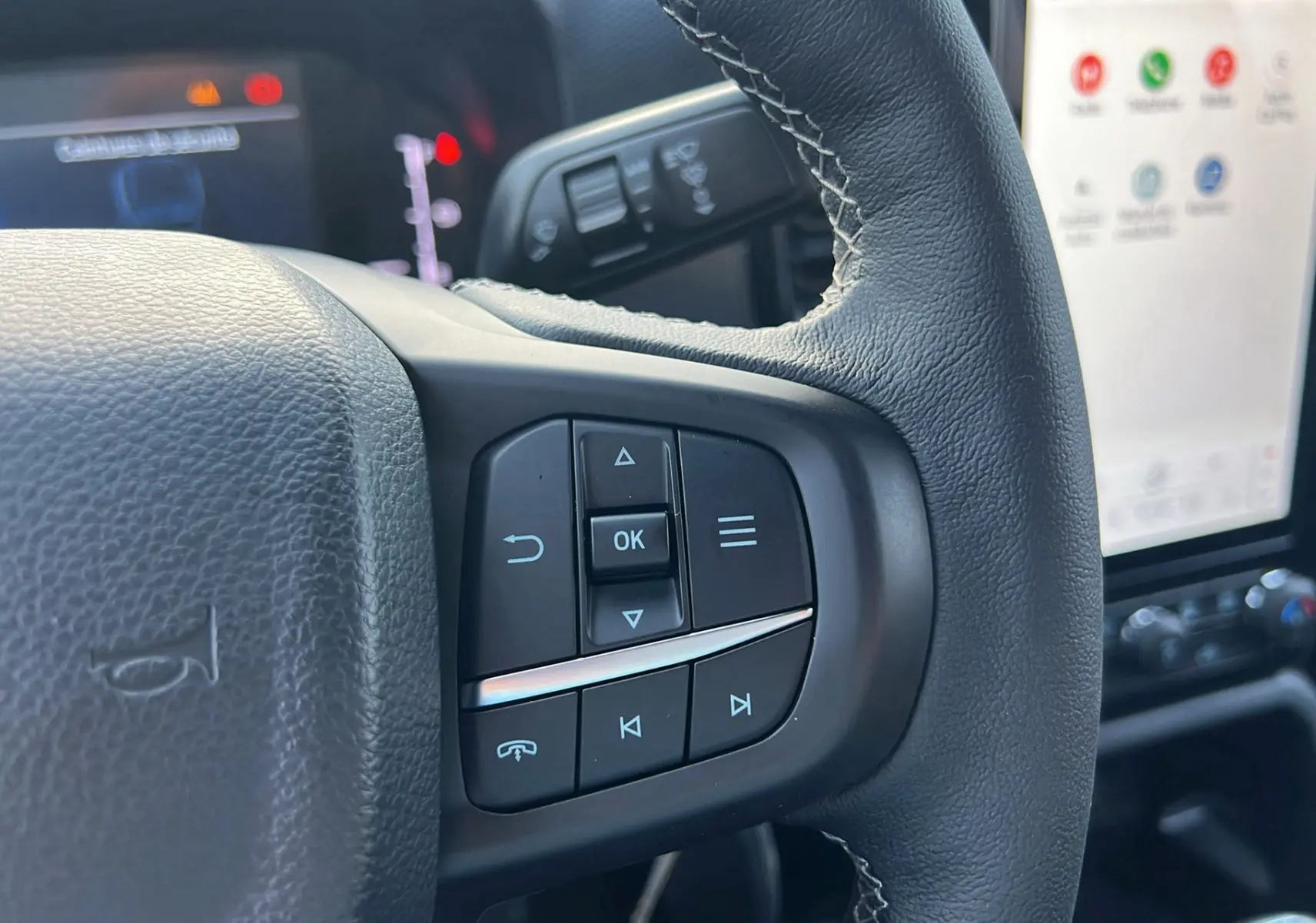 Gros plan sur les commandes au volant cuir du Ford Ranger 2025, avec écran tactile multifonction en arrière-plan.