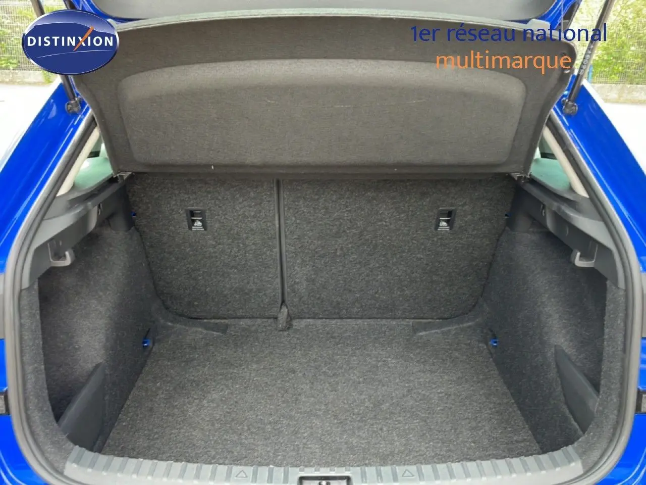 Coffre ouvert vu de l’arrière d’une Skoda Scala 2025 en bleu racing metal, intérieur du coffre en tissu gris.