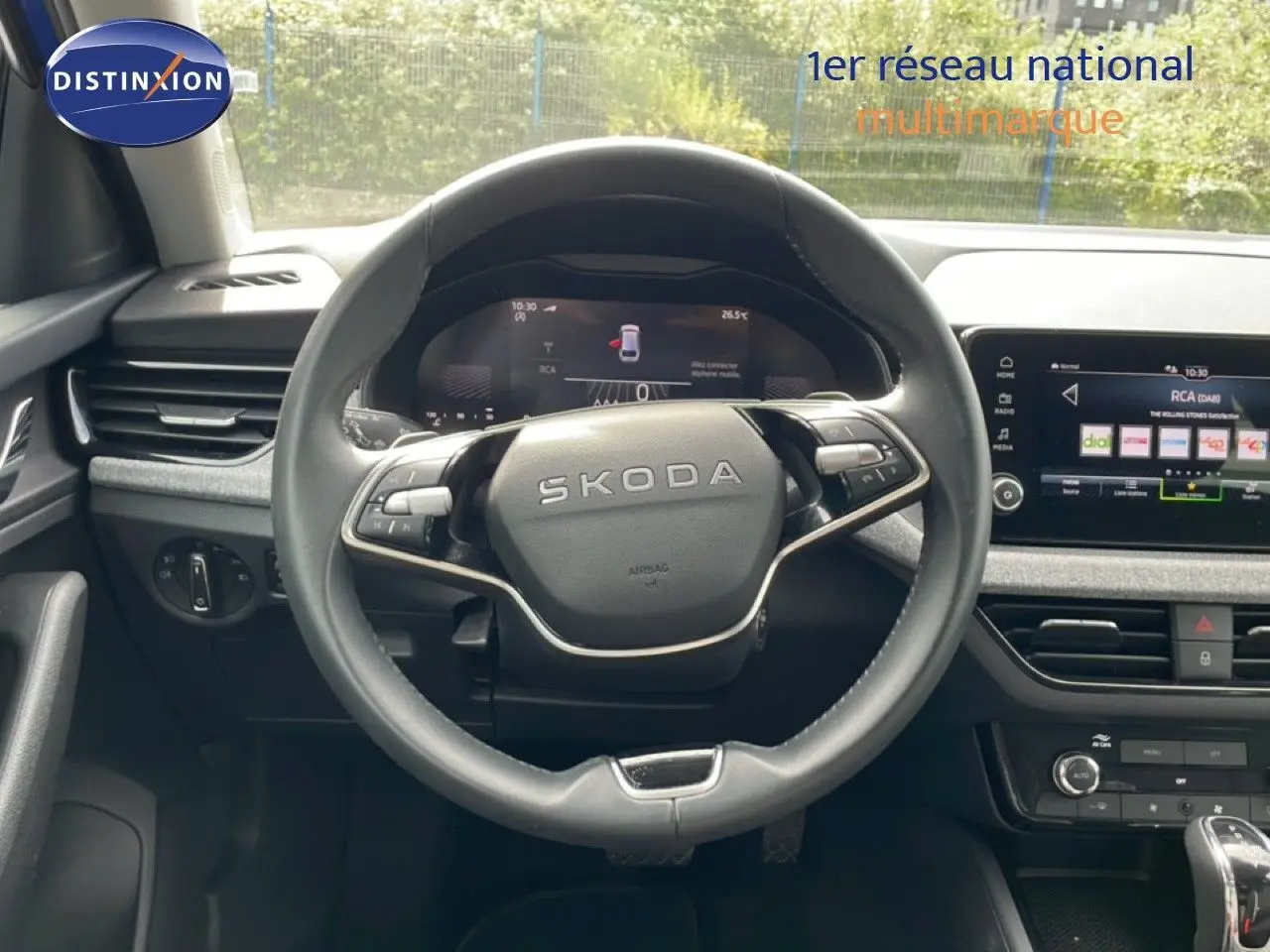 Vue intérieure centrée sur le volant SKODA d'une Scala 2025, avec tableau de bord digital et écran tactile multimédia.