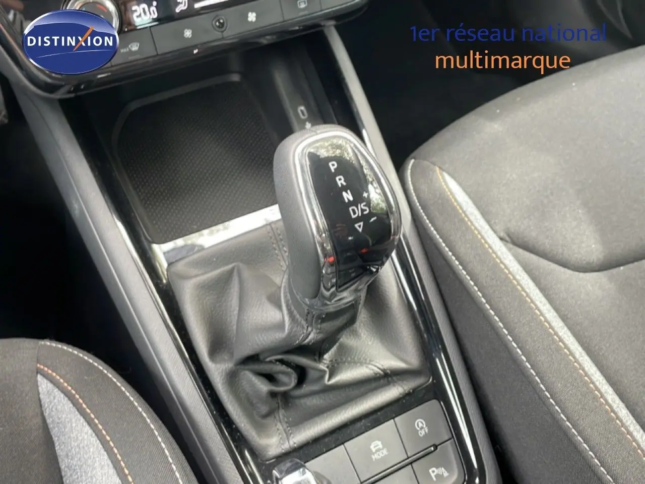 Gros plan sur la console centrale de la Skoda Scala 2025, boîte auto avec levier en cuir et sièges tissu gris noir.