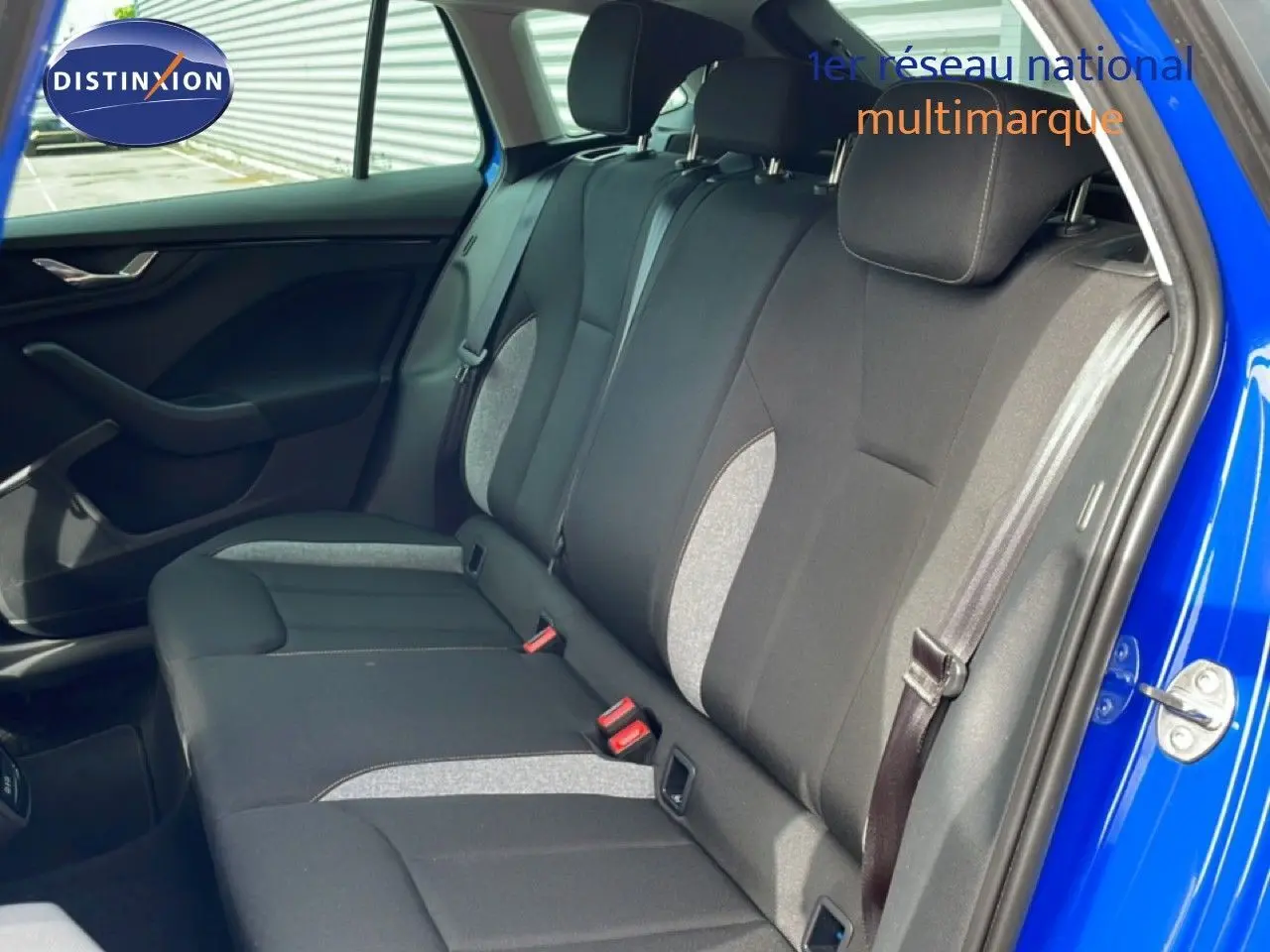Vue intérieure sur la banquette arrière en tissu gris et noir d'une Skoda Scala bleu racing, porte arrière ouverte côté droit.