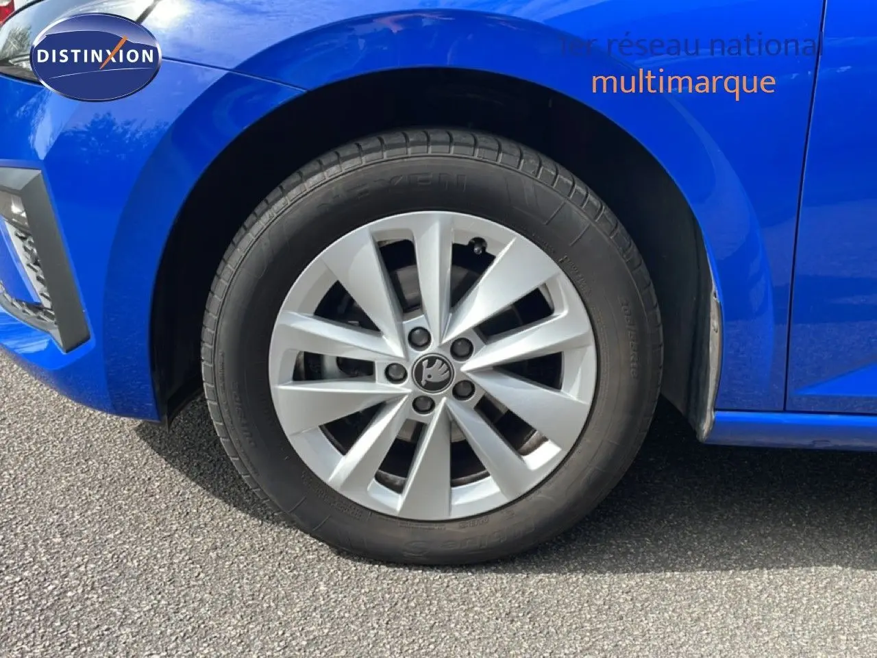 Gros plan sur la roue avant gauche d'une Skoda Scala bleu racing metal, mettant en valeur la jante argentée au design moderne.