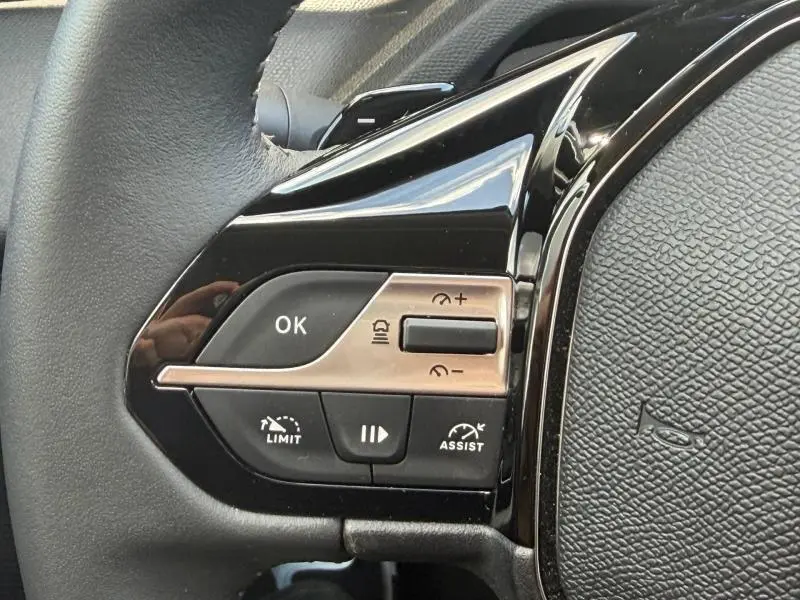 Gros plan sur les commandes du volant côté gauche du Peugeot 308 SW 2025, finition noire brillante et boutons multifonctions.