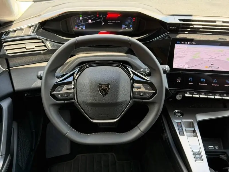 Vue frontale du poste de conduite du Peugeot 308 SW 2025 avec volant compact, tableau de bord numérique et écran tactile central.